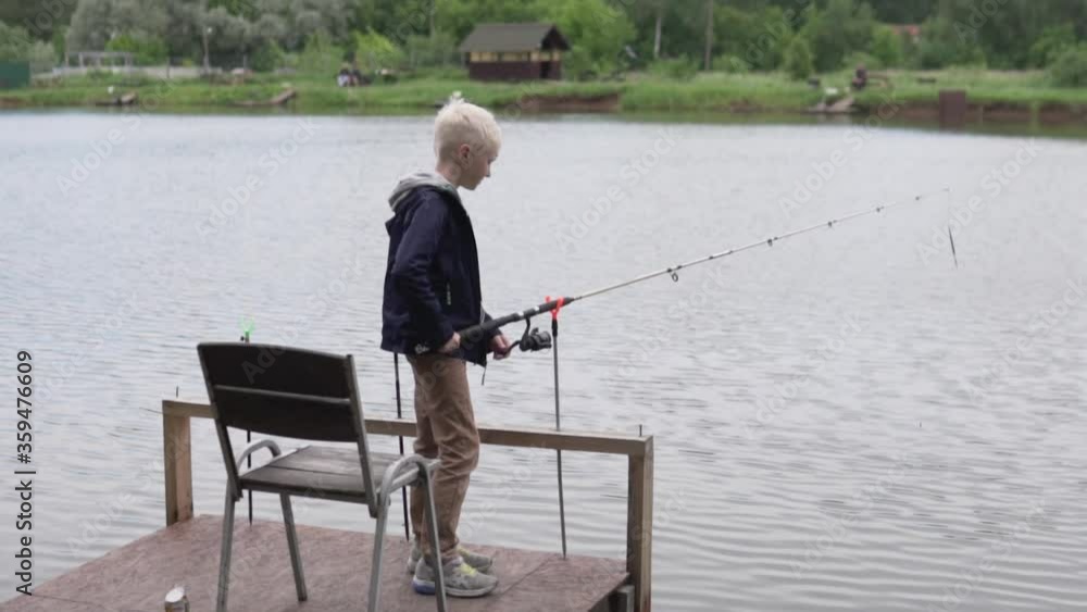 A beautiful boy blond fish fishing rod on the pier by the lake in the summer. A beautiful boy blond fish fishing rod on the pier by the lake in the summer.