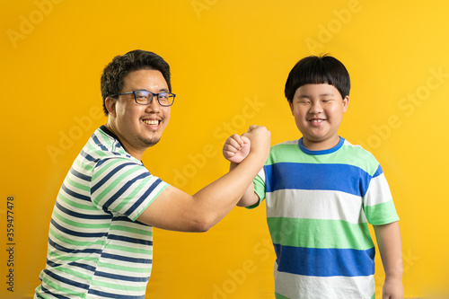 the cross-arm gesture of Asian father and child, successful cooperation of generations, yellow background