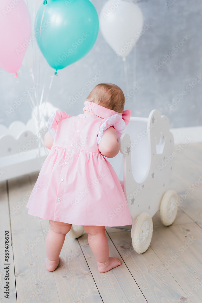 Girl in a pink dress and balloons celebrates her first birthday
