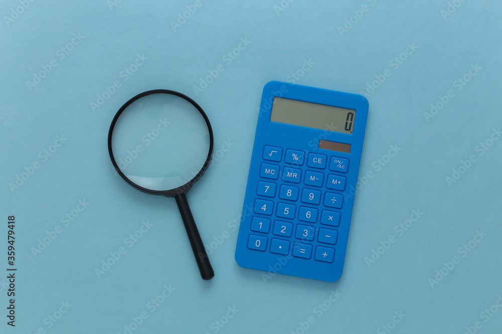 Calculator with a magnifier on a blue background. Top view Calculator with a magnifier on a blue background. Top view