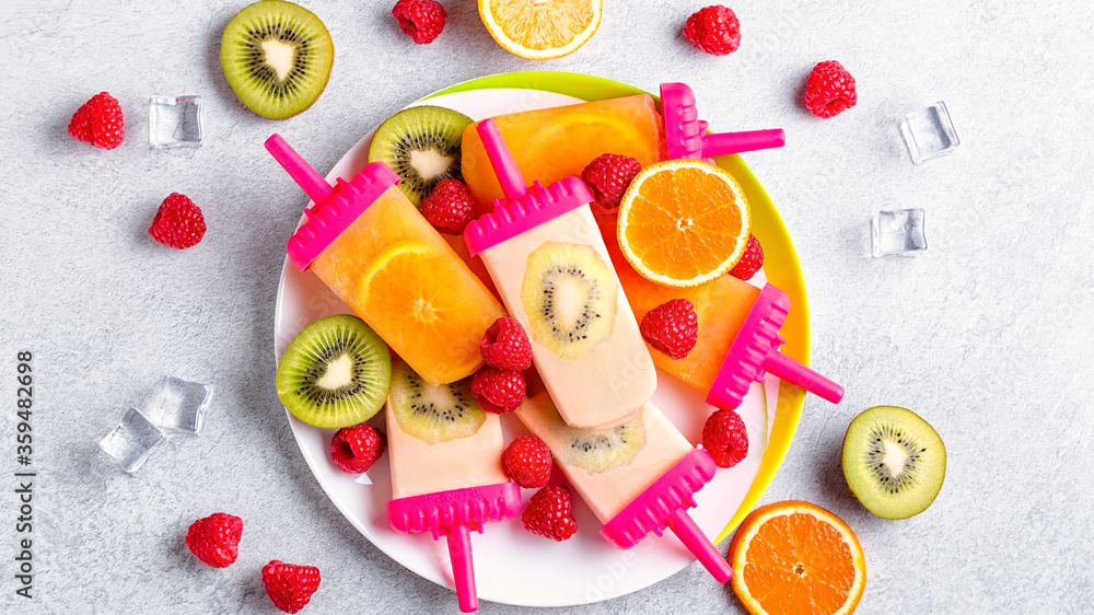 Summer refreshing homemade popsicles with oranges and kiwi. Healthy snack with fruits and frozen juice for summer heat on concrete table top, flat lay, copy space