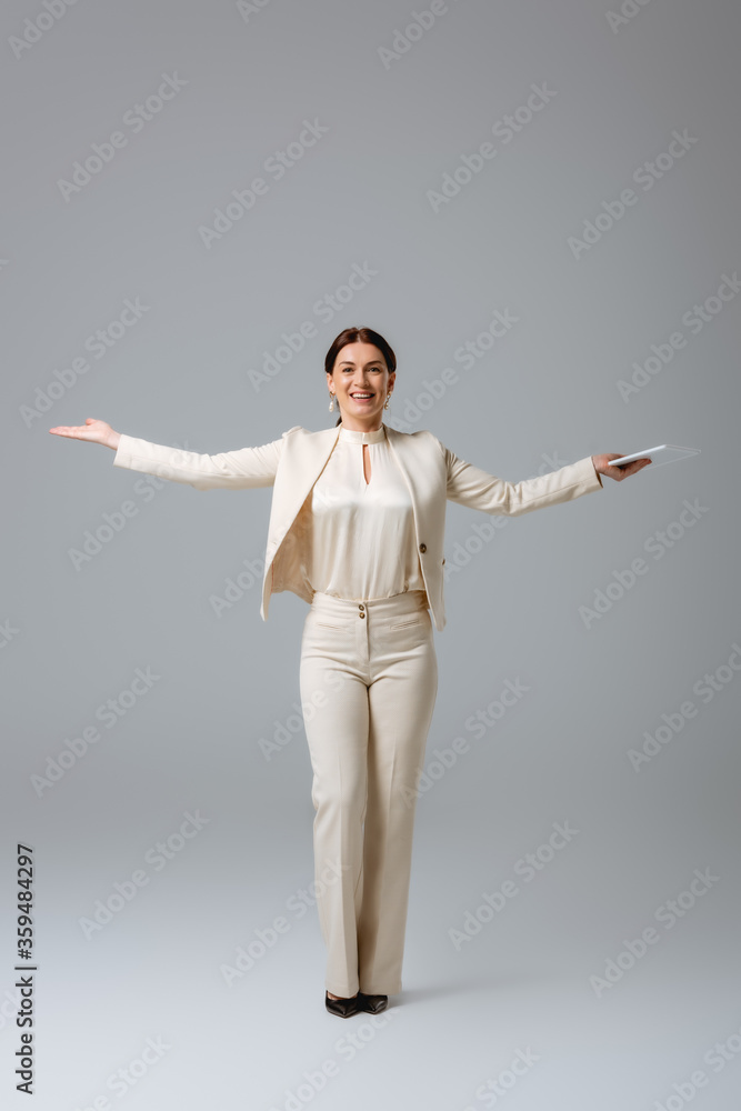Positive businesswoman pointing with hand and holding digital tablet on grey background, concept of body positive Positive businesswoman pointing with hand and holding digital tablet on grey background, concept of body positive