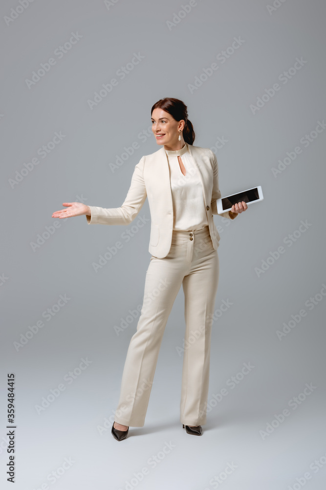 Smiling businesswoman pointing with hand and holding digital tablet on grey background Smiling businesswoman pointing with hand and holding digital tablet on grey background