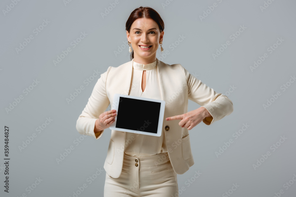 Beautiful smiling businesswoman pointing with finger at digital tablet isolated on grey Beautiful smiling businesswoman pointing with finger at digital tablet isolated on grey