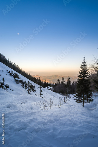 Snowy landscape in mountains. Golden hour sunset with visible moon in the sky. Winter season in Alps, Slovenia. Late evening hiking