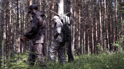 Two hunter men in camouflage clothes with guns walking through forest during hunting season. Man hunter outdoor in forest hunting. Male Tourists