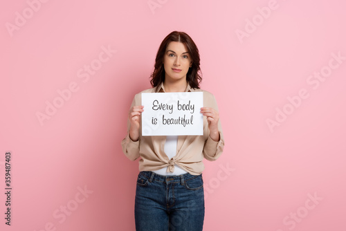 Fototapete Beautiful woman holding card with every body is beautiful lettering on pink back