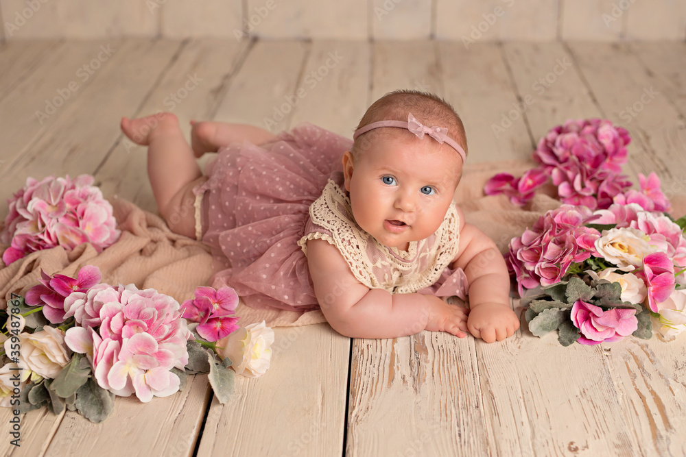 Happy smiling baby girl in a pink dress lies on her stomach on a white wooden background with gems... Happy smiling baby girl in a pink dress lies on her stomach on a white wooden background with gems...