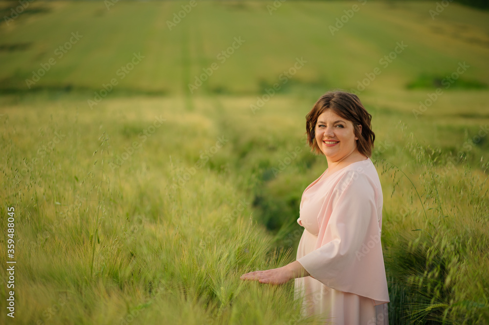 Portrait of a overweight woman in a pink dress. A woman is standing in a green wheat field. Portrait of a overweight woman in a pink dress. A woman is standing in a green wheat field.