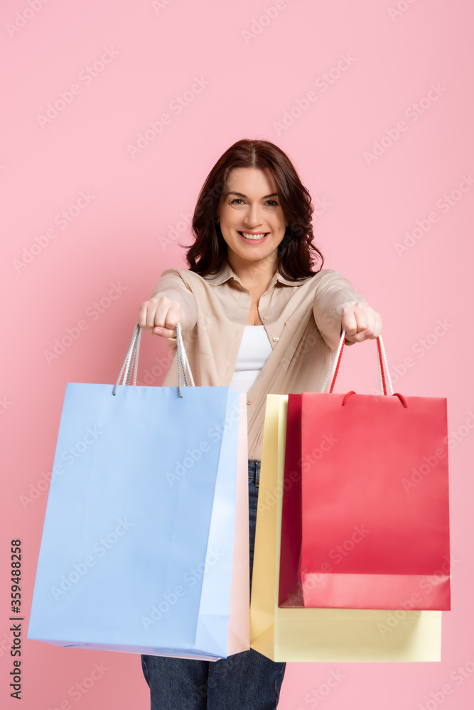 Happy brunette woman smiling at camera and showing shopping bags on pink background Happy brunette woman smiling at camera and showing shopping bags on pink background