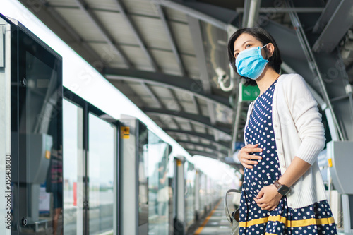 Asian Pregnant Woman in face mask waiting commuter train for traveling to work.