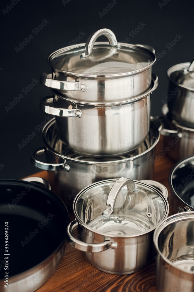 Set of kitchen metallic pans standing on wooden countertop on dark background
