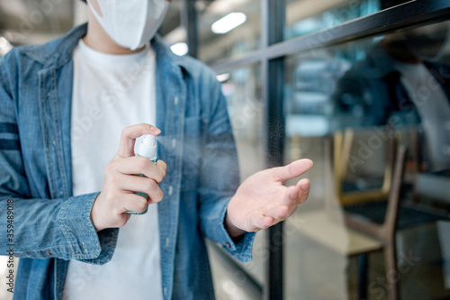 Cleaning hands with sanitizer spray. Asian man wearing mask spraying alcohol to prevent Coronavirus (COVID-19) infection in public area. Health care with antibacterial product.