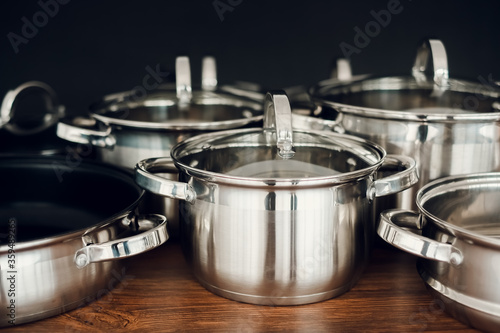 Set of kitchen metallic pans standing on wooden countertop on dark background