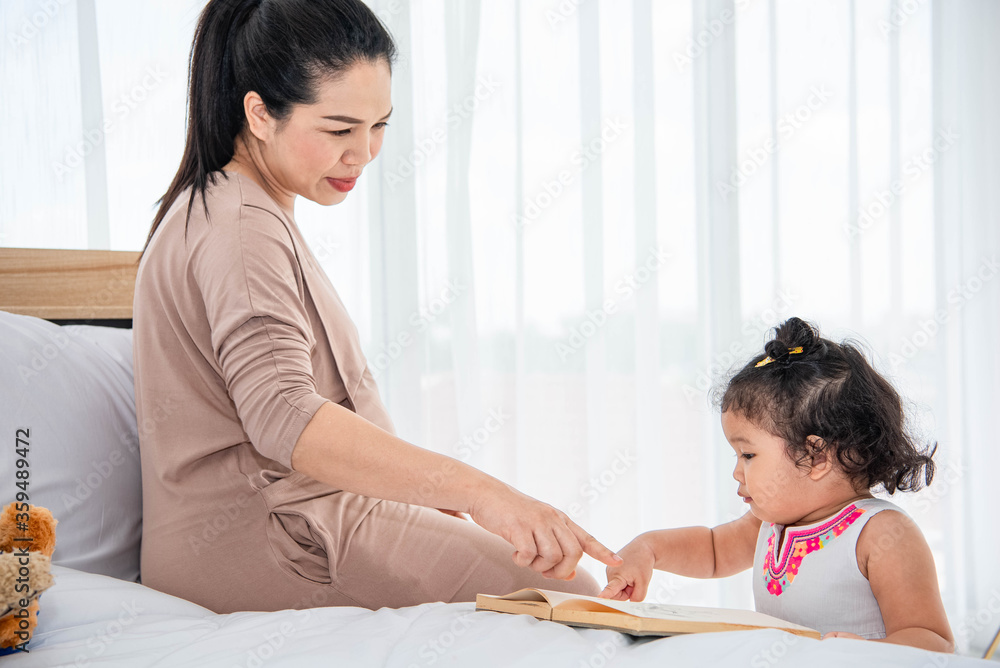 Asian mother teaching girls daughter to reading books in house Asian mother teaching girls daughter to reading books in house