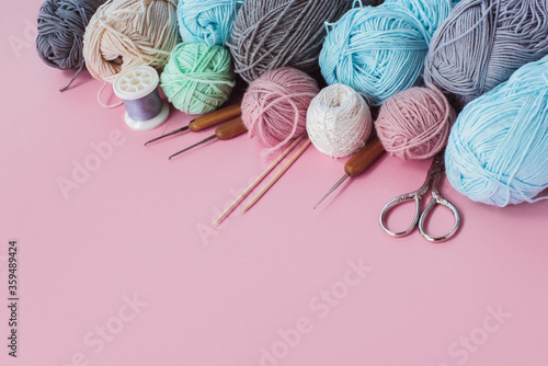 Women's hobby. Multicolored skeins, needles, hooks on the pink background. Conept of sewing, crochet and knitting. 