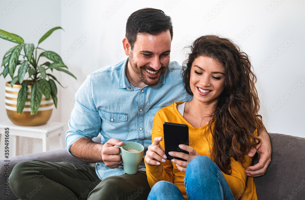 Happy smiling couple embracing and looking at smart phone at home stock photo Happy smiling couple embracing and looking at smart phone at home stock photo