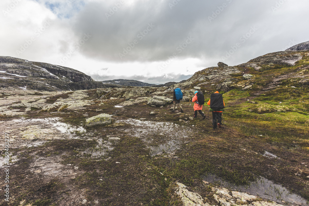 Tourists with backpacks walk across a rocky plain to the famous landmark - Troll tongue rock or Trolltunga. Cold and windy summer in Norway.