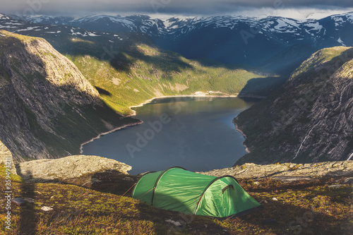 Tourist's tent stands in the mountains near famous landmark - Troll tongue rock or Trolltunga. Sunrise above beautiful fjord in Norway.