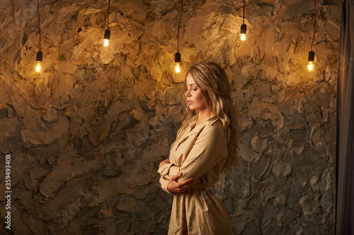Side portrait of blond charming woman against light loft wall photo