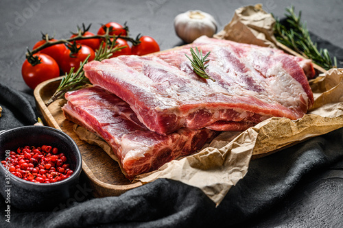 raw pork meat ribs with ingredients for cooking rosemary and garlic in a wooden bowl. Black background. Top view
