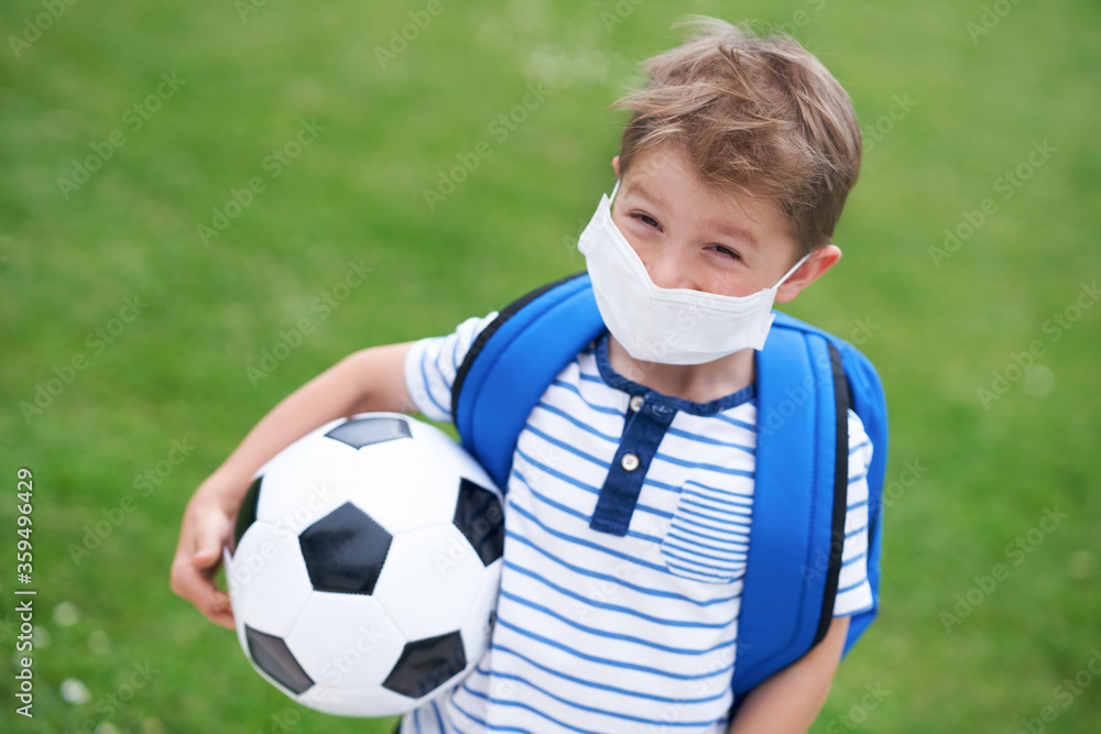 Naklejka premium Adorable little boy with football and protective mask on the field