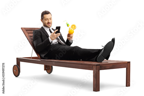 Fotografia Guy in a suit holding a cocktail and using a mobile phone while lying on a sunbe