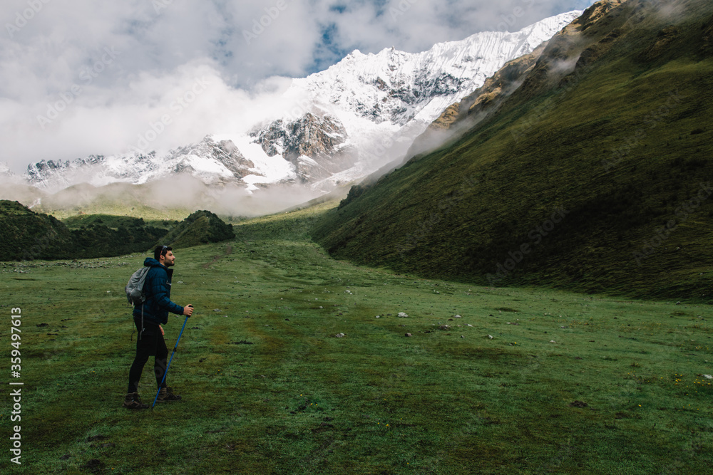 Side view of professional traveller with backpack travelling using trackking sticks enjoying wanderlust in Salkantay Peru.Young man tourist hiking on green landscape of hight mountains