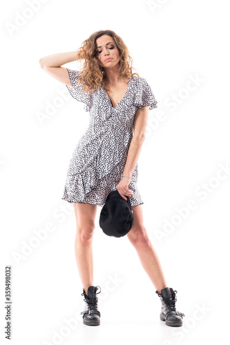 Young emotional and disappointed stylish woman looking down with hand in hair holding cap. Full length portrait isolated on white background. 