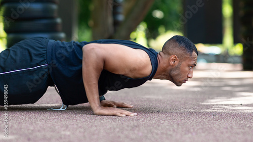 Side view of muscular black guy working out outdoors, doing push up exercises at park