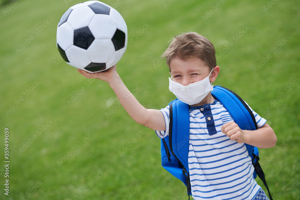 Obraz premium Adorable little boy with football and protective mask on the field