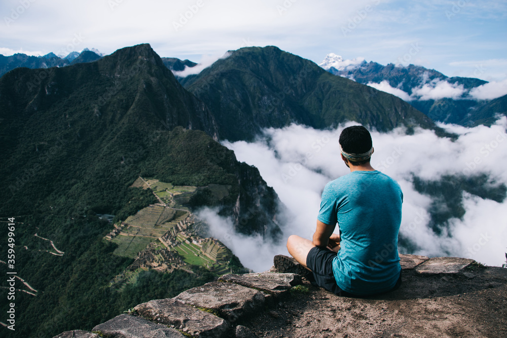Back view of professional man dressed in active wear resting on peak of mountain and admiring green hills of Machu Picchu and breathtaking scenery of natural environment during trekking wanderlust
