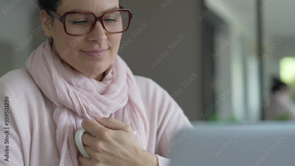 Smiling woman with dark hair drinking hot tea while connected on laptop computer Smiling woman with dark hair drinking hot tea while connected on laptop computer