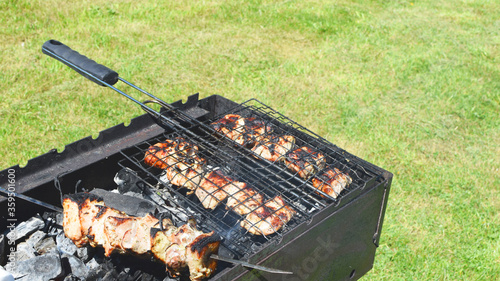 Skewers with meat on hot grill closeup outdoors on green grass background. Concept of summer grilling, picnic, barbecue. 