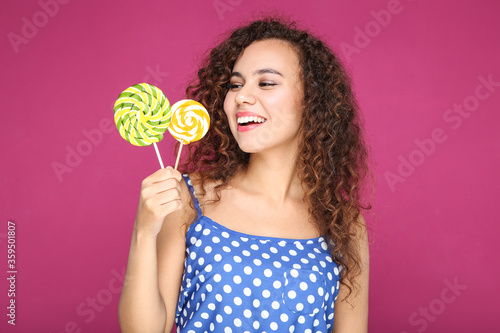 Young american girl with colorful lollipops on pink background