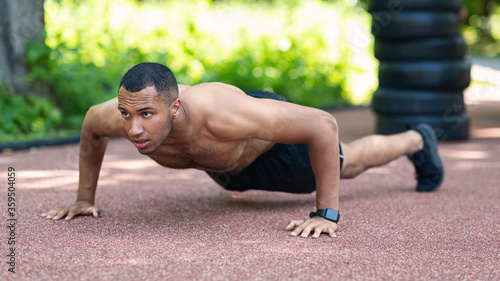 Shirtless muscular black guy performing push ups on jogging track at city park
