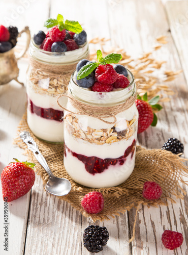 Tasty yoghurts with muesli, fresh berries and jam on wooden table. Healthy breakfast.