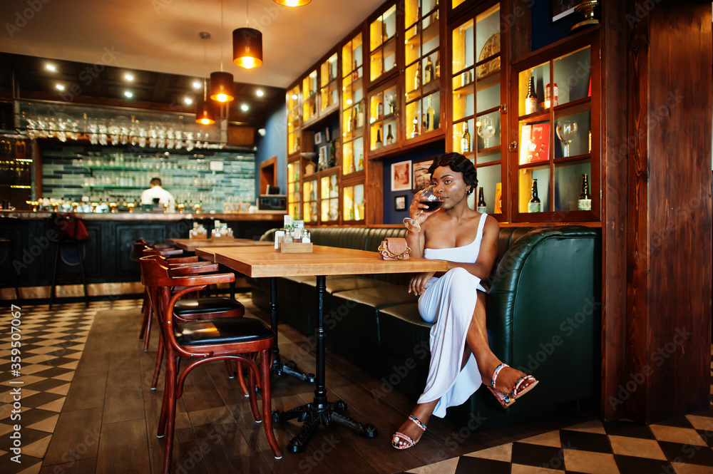 African american woman, retro hairstyle in white dress at restaurant with glass of wine. African american woman, retro hairstyle in white dress at restaurant with glass of wine.