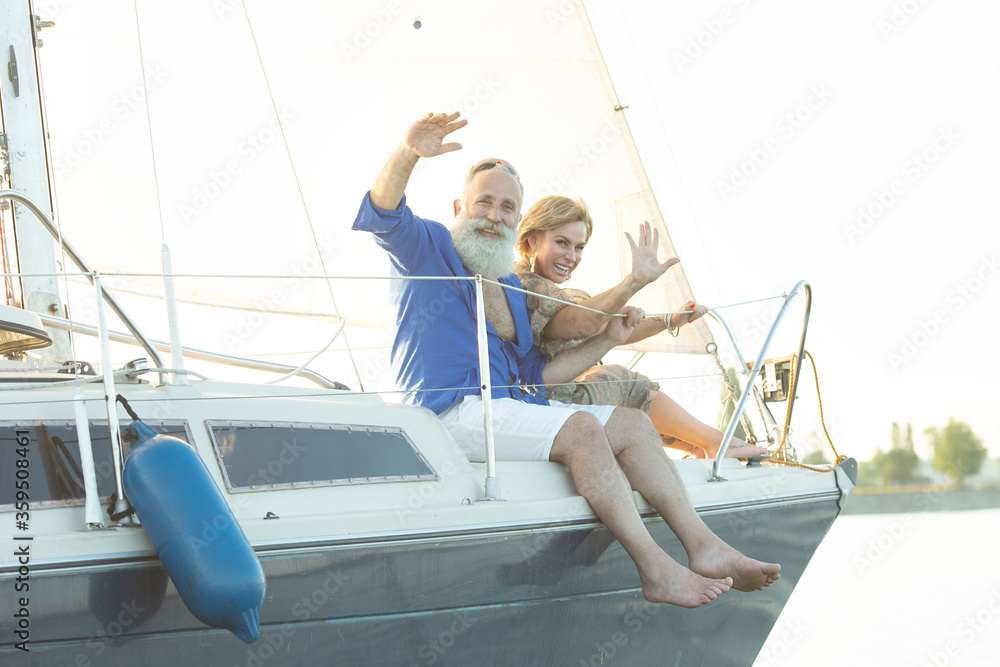 A happy senior couple sailing and sitting at the wheel of a sail boat on lake.