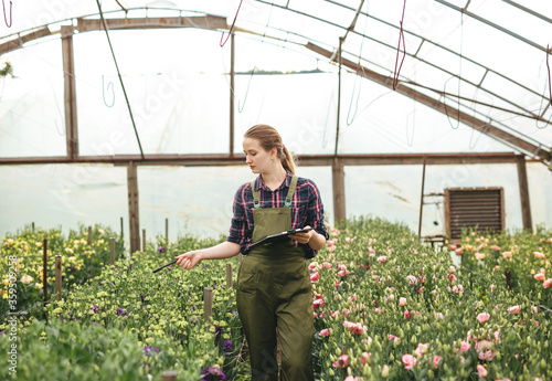 Gardener woman working on flowers in greenhouse  and makes notes. Floral business concept.