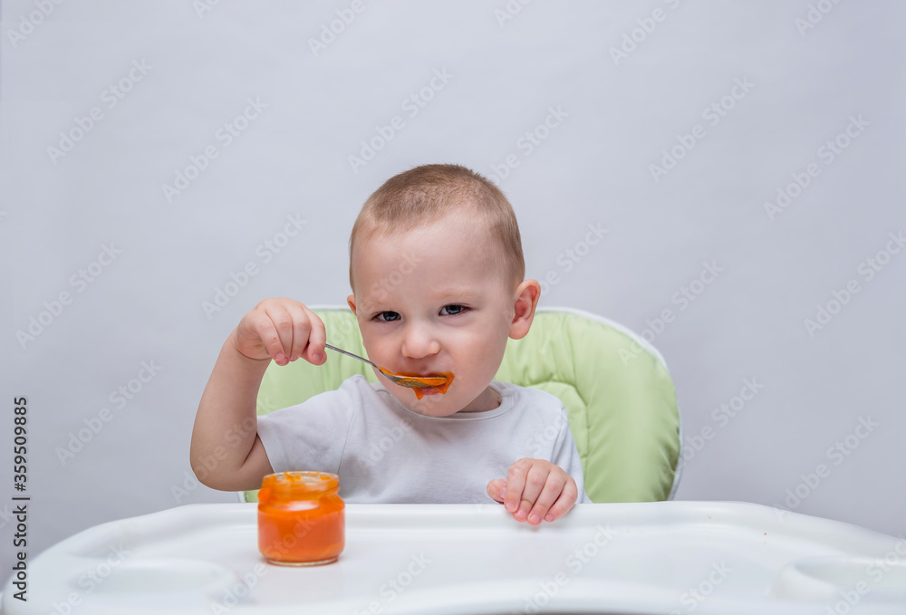 a small boy eats mashed carrots at a table and looks at the camera on a white isolated background with space for text a small boy eats mashed carrots at a table and looks at the camera on a white isolated background with space for text