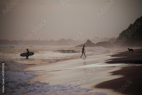 silhouettes of young surfers on the coastline while the golden hour before sunset, black sand beach