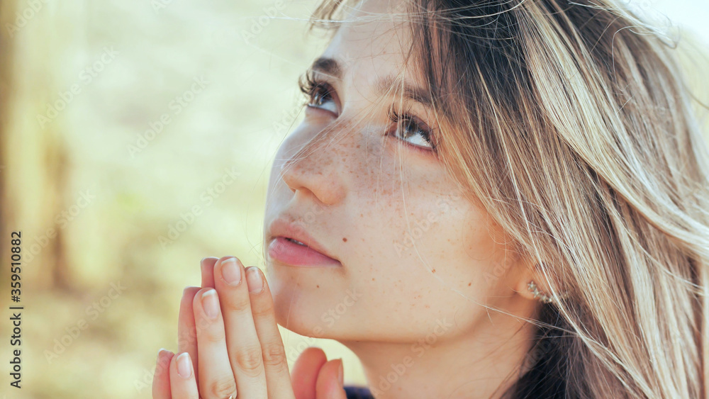 A young blonde 18 year old girl prays with folded hands. A young blonde 18 year old girl prays with folded hands.