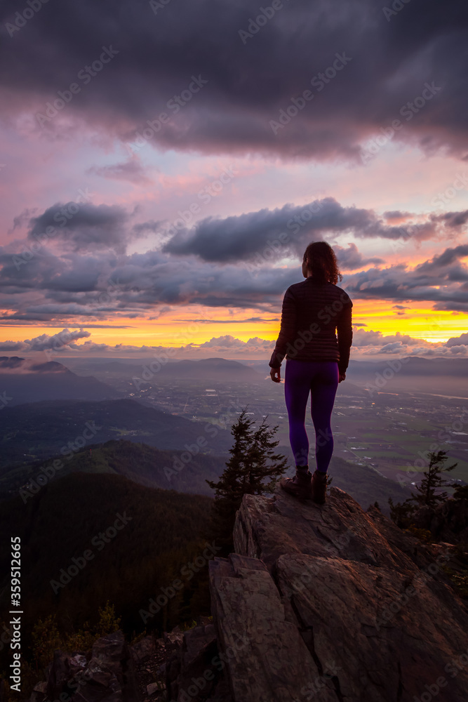 Obraz premium Adventurous Girl on top of a Rocky Mountain overlooking the beautiful Canadian Nature Landscape during a dramatic Sunset. Taken in Chilliwack, East of Vancouver, British Columbia, Canada.