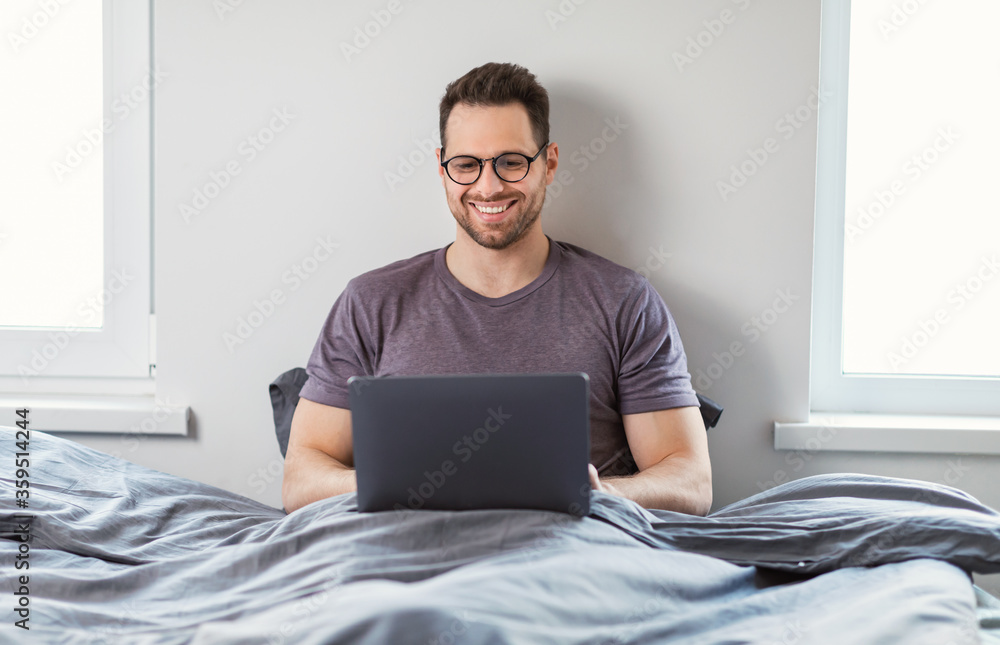 Man With Laptop Working Online From Home Sitting In Bed Man With Laptop Working Online From Home Sitting In Bed