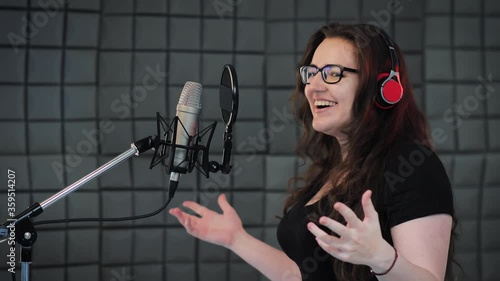 Female person records POP song at the recording studio. Singer emotionally gesturing with her hands. Soundproof room for professional recording vocal