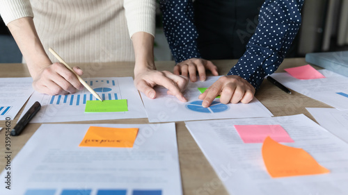 Close up businesswomen analyzing project stats reviewing information and data on charts shown on papers financial report, make overview attach post-it writing notes, explanations, forecasting concept