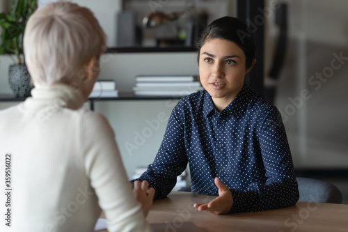 Multi ethnic indian and caucasian diverse young businesswomen sitting in front of each other in office during business meeting. HR manager and vacancy candidate talk, job interview and hiring concept