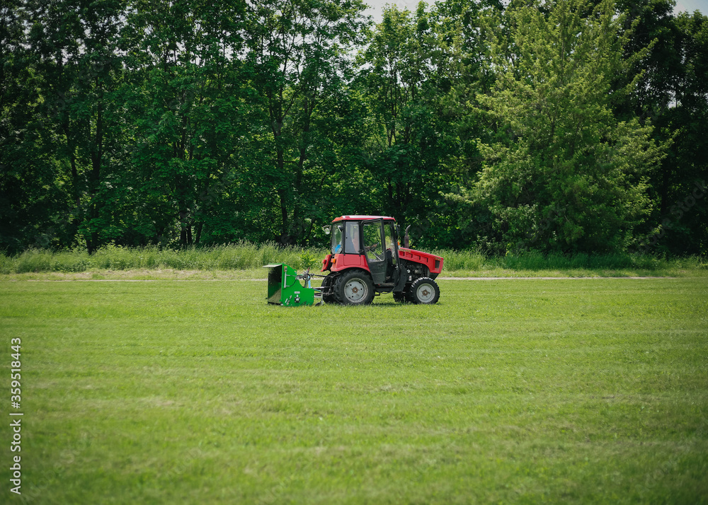 A tractor mows grass in a summer park. A tractor mows grass in a summer park.