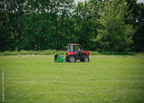 A tractor mows grass in a summer park.